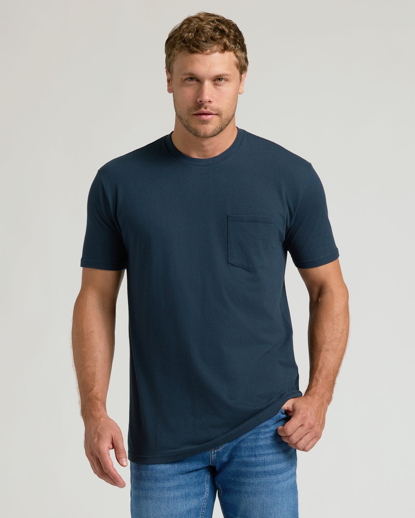Model in Navy Pocket Crew Tee and jeans, adjusting shirt hem.