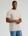 Man wearing a beige t-shirt and blue jeans on a plain background