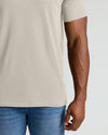 Person wearing a beige t-shirt and blue jeans on a plain background