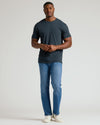 Man wearing a dark gray t-shirt and blue jeans on a white background