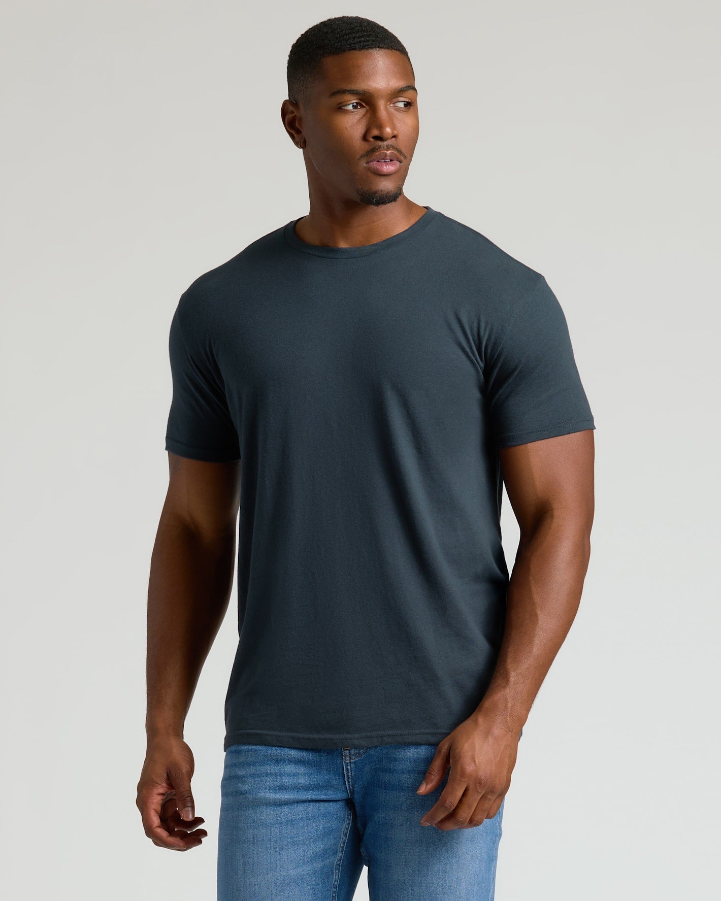 Man wearing a dark gray t-shirt and blue jeans on a light gray background