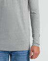Close-up of a person wearing a light heather gray long-sleeve top with blue jeans against a plain light gray background.