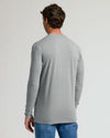 A man viewed from the back wearing a light gray long-sleeve t-shirt and blue jeans, standing against a plain light gray studio background.
