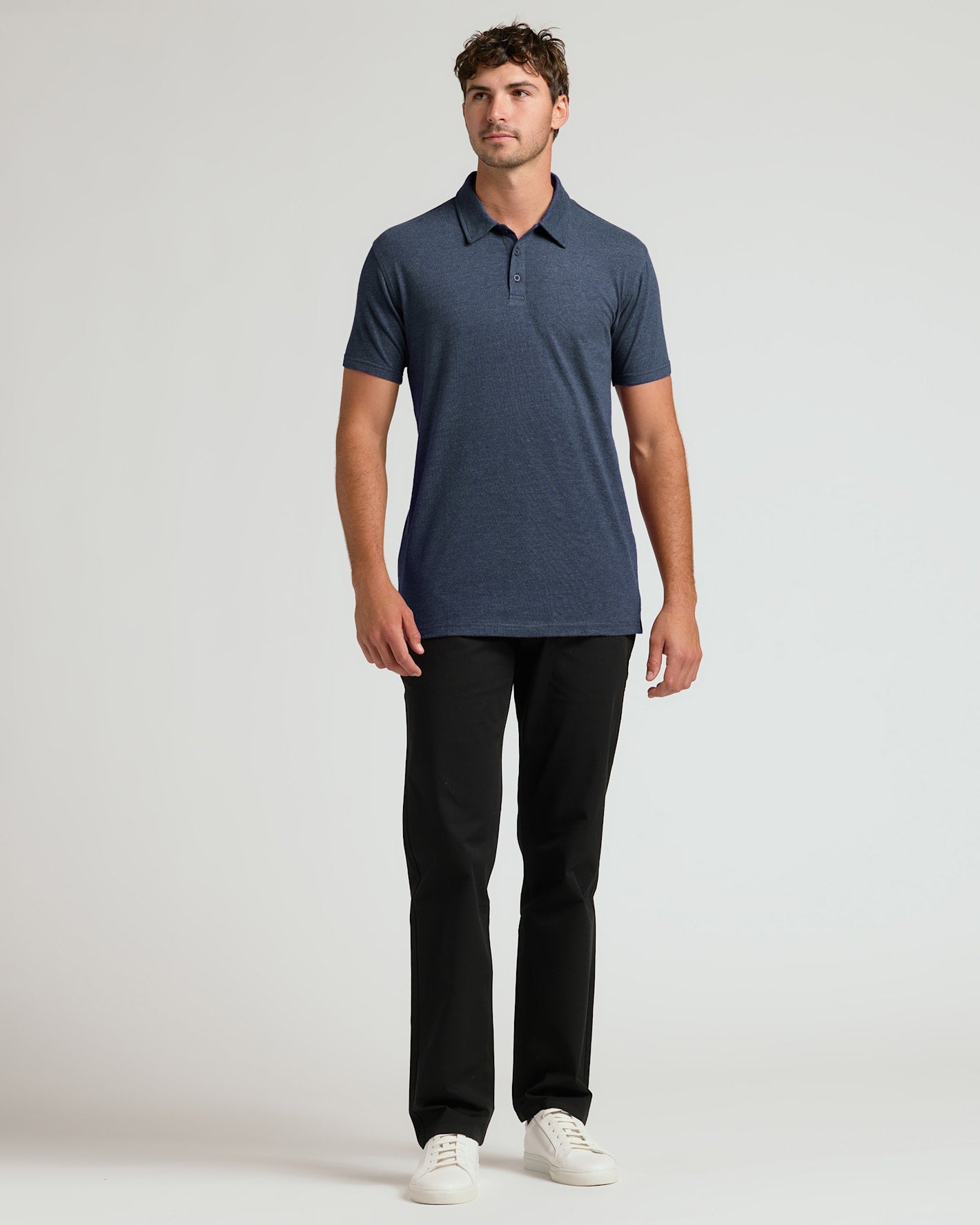 Man wearing a navy blue polo shirt and black pants on a light gray background