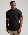 A man wearing a black short-sleeve polo shirt and khaki pants, standing against a light gray studio background.