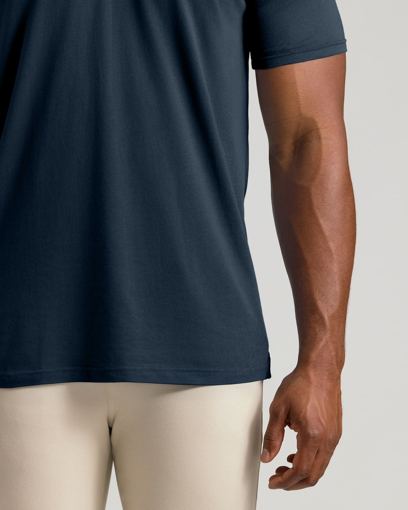 Close-up of a person wearing a dark navy short-sleeve athletic t-shirt and light beige compression leggings against a light gray studio background.