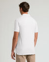 A man viewed from the back wearing a white short-sleeve polo shirt and khaki pants against a light gray studio background.