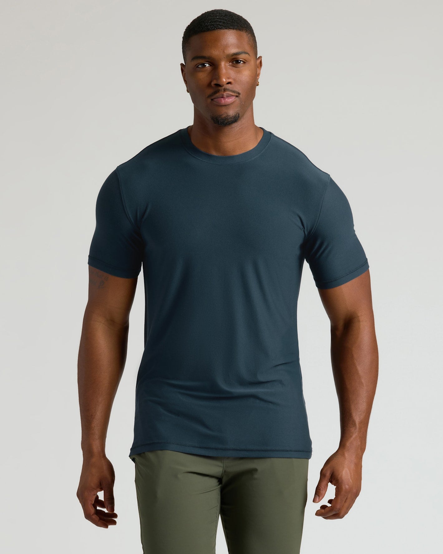 Man wearing a dark blue t-shirt and green pants on a light gray background