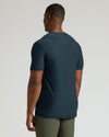 Man wearing a dark blue t-shirt and green pants on a light gray background