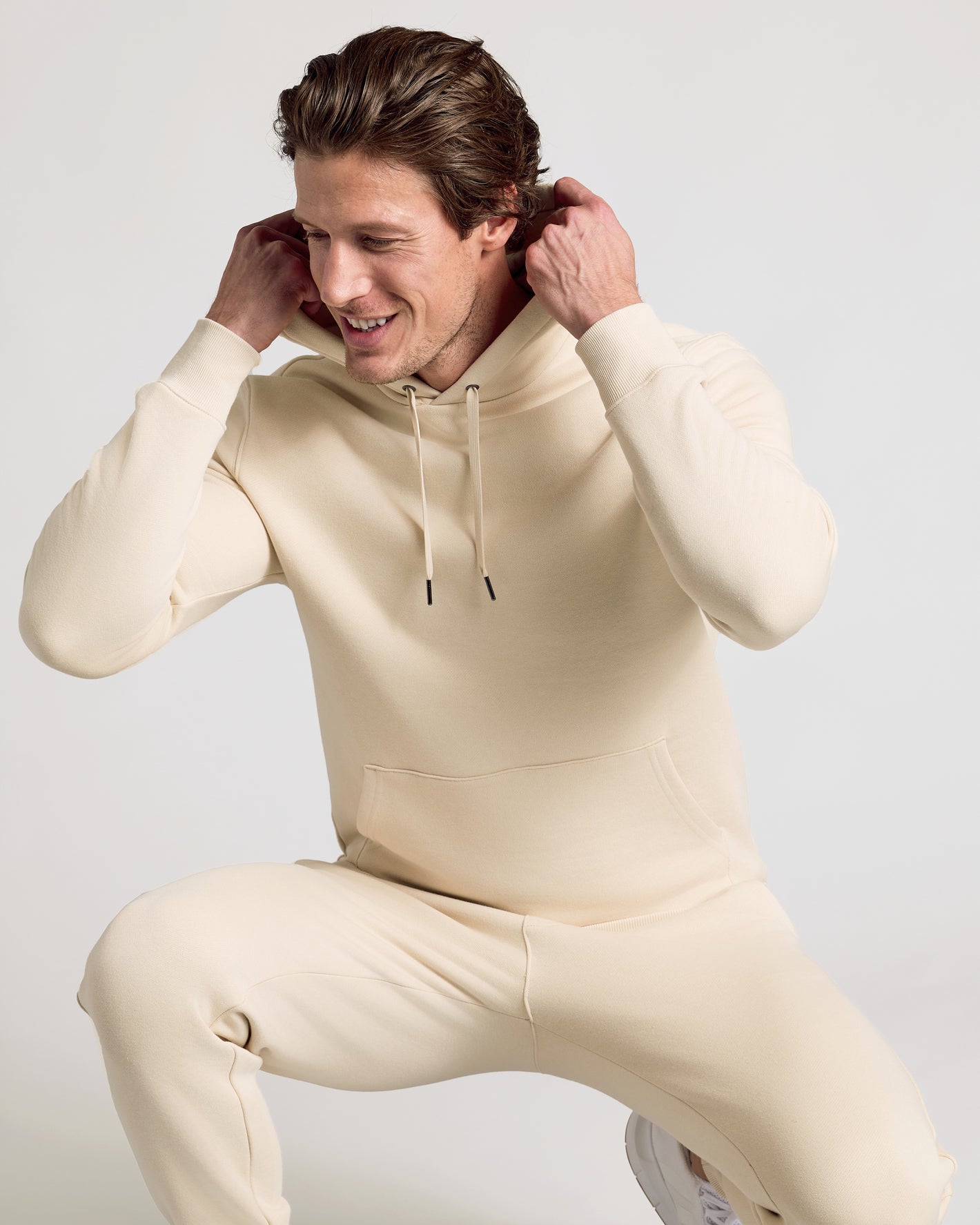 Man wearing Dune Fleece French Terry Pullover Hoodie, adjusting hood.