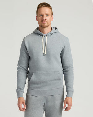 A man wearing a Dark Heather Gray Fleece French Terry Pullover Hoodie with a front kangaroo pocket and adjustable cream-colored drawstrings, styled as men's basics.