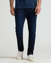 A person wearing slim-fit dark blue denim jeans and white sneakers, shown from the waist down against a plain light gray studio background.