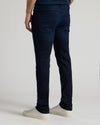 Rear view of a person wearing dark navy blue slim-fit jeans and white sneakers against a light gray studio background.