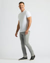 Man wearing Gray Medium Indigo Slim Comfort Stretch Jeans 3-Pack with a white t-shirt and black sneakers, standing against a plain light background in a relaxed pose.