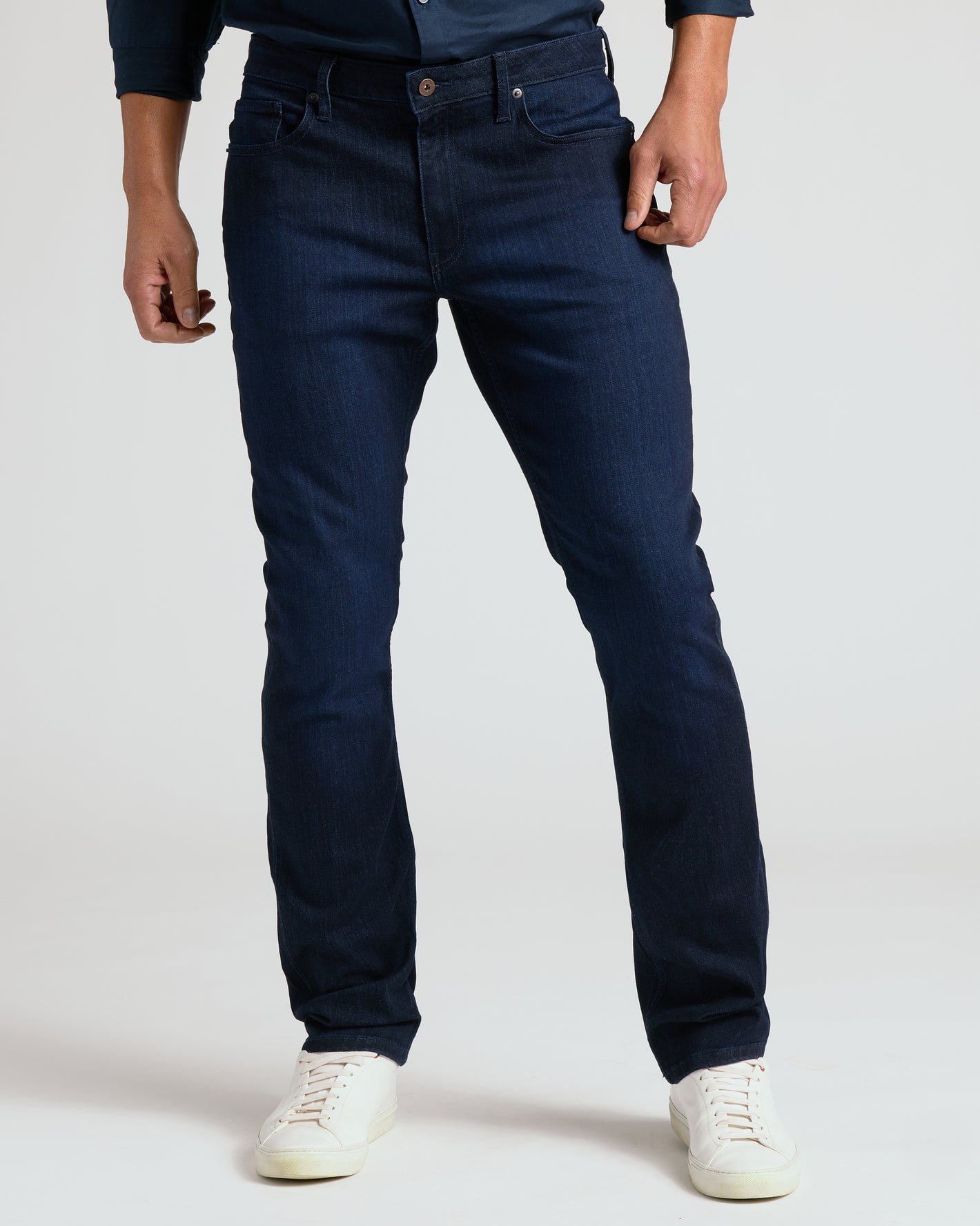 Person wearing dark blue jeans and white sneakers on a plain background