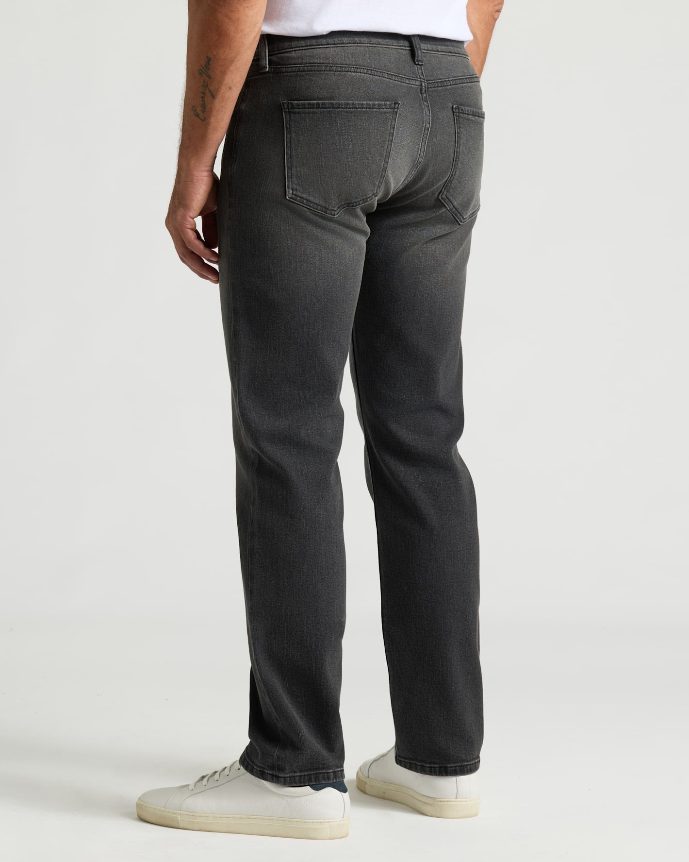 Gray Wash Straight Authentic Denim Jeans with white sneakers and tattooed forearm.