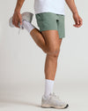 Person stretching in olive-green Seasonal Active Quick Dry Short with light grey sneakers.