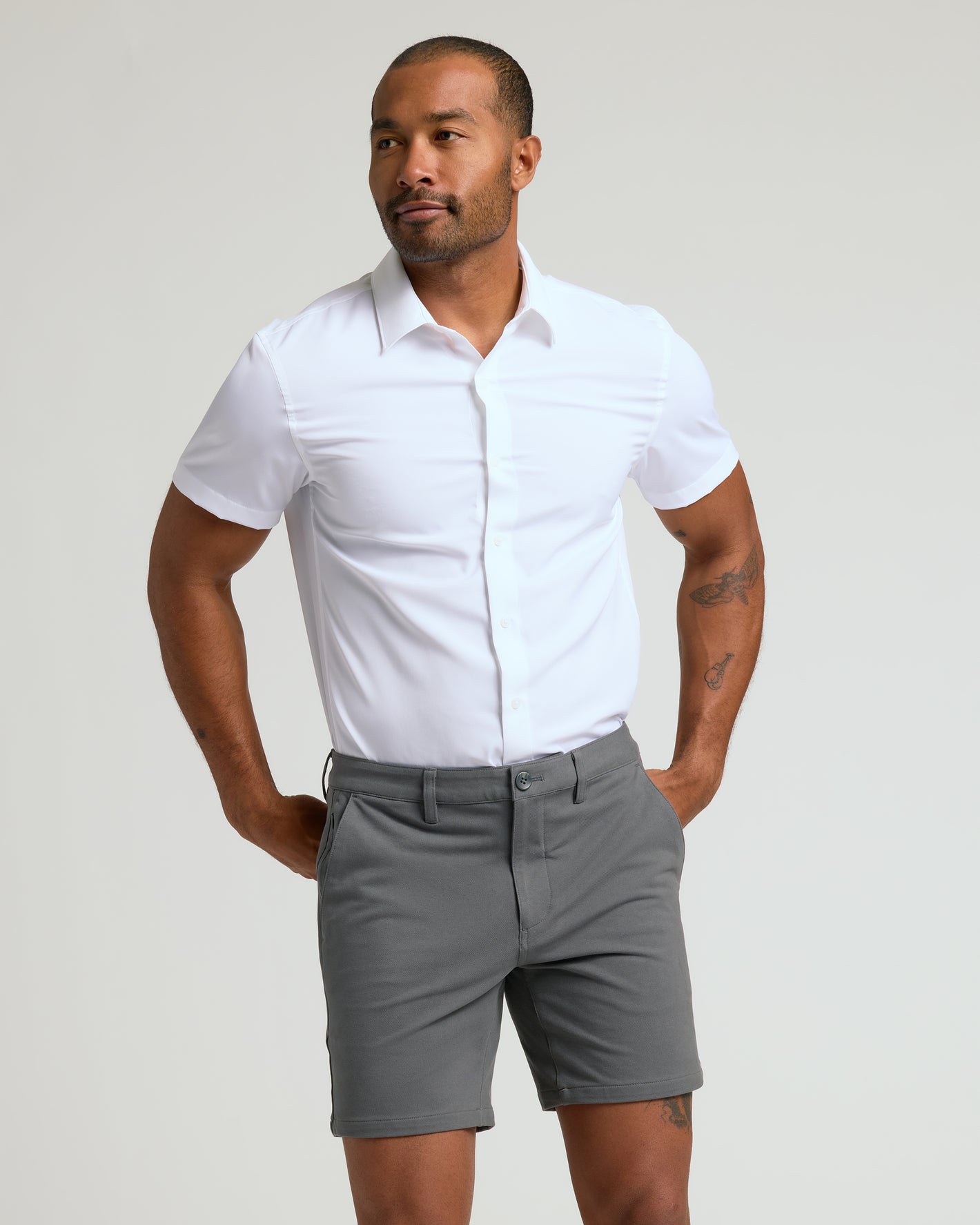 Man wearing 7 Carbon Chino Shorts 2.0 with white shirt, hands in pockets.