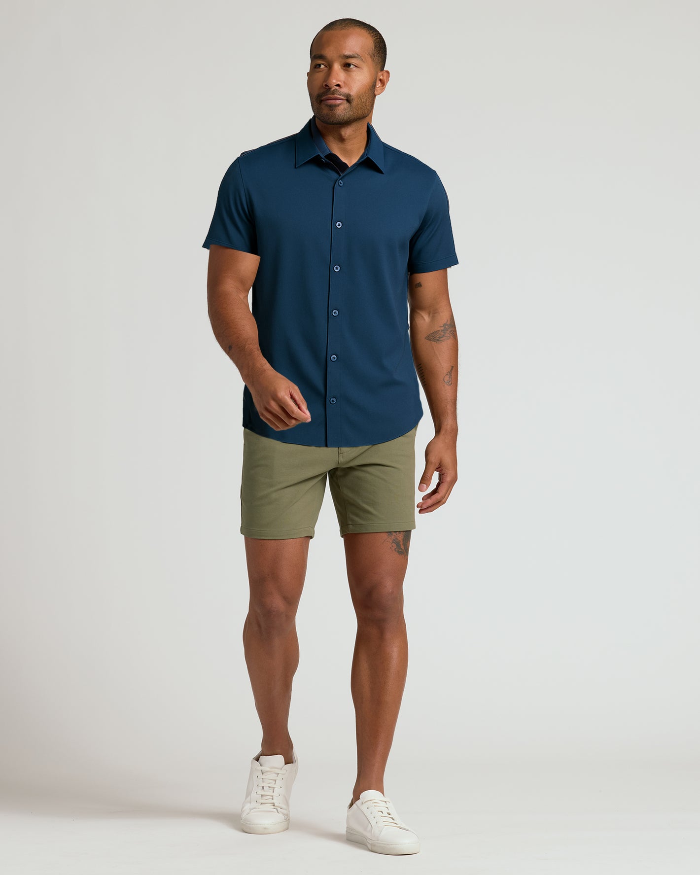 Model wearing 7 Military Green Classic Chino Shorts, mid-stride, tattoos visible.