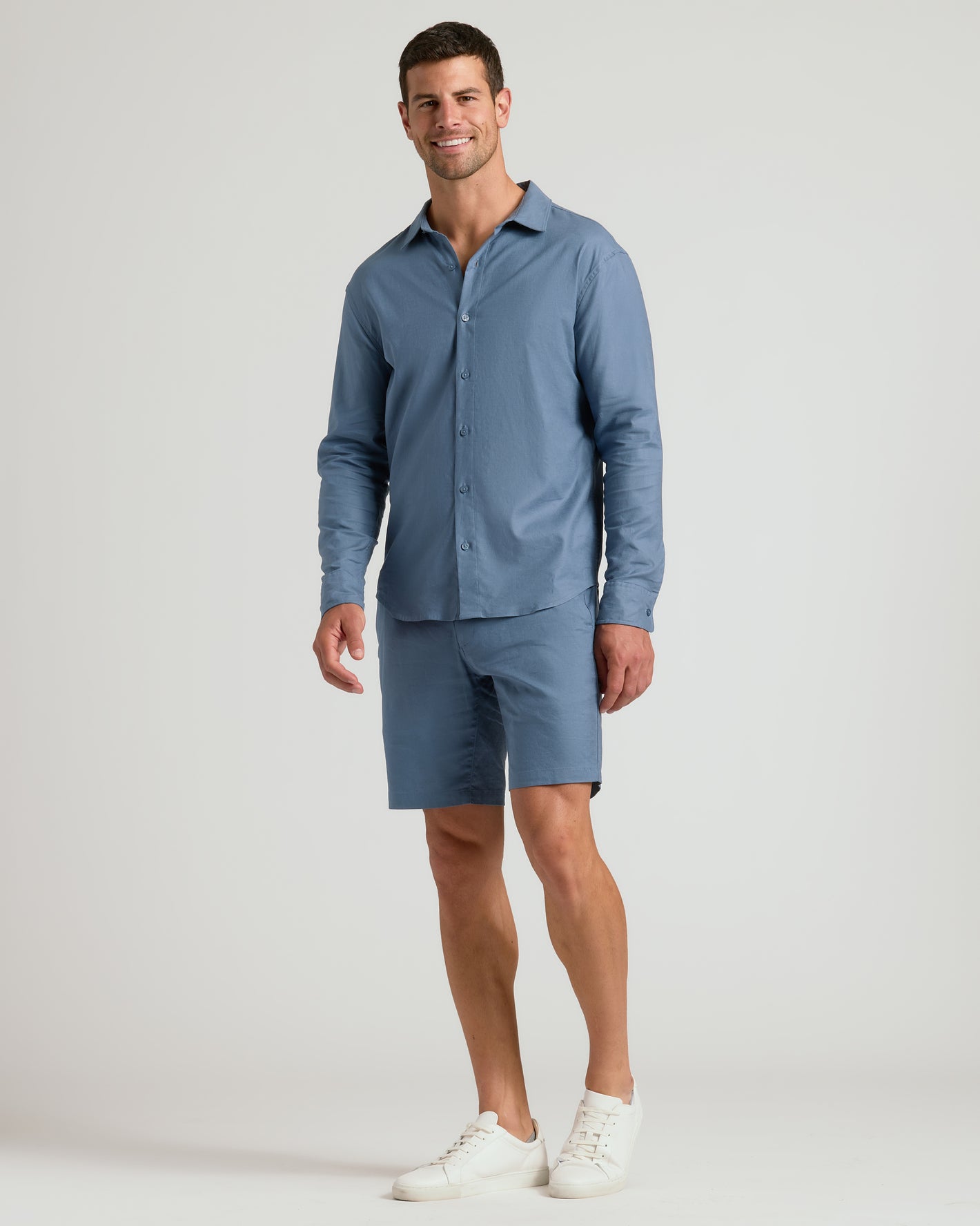 Model in 9 Fiord Linen Shorts, slate-blue, casual pose, white sneakers.