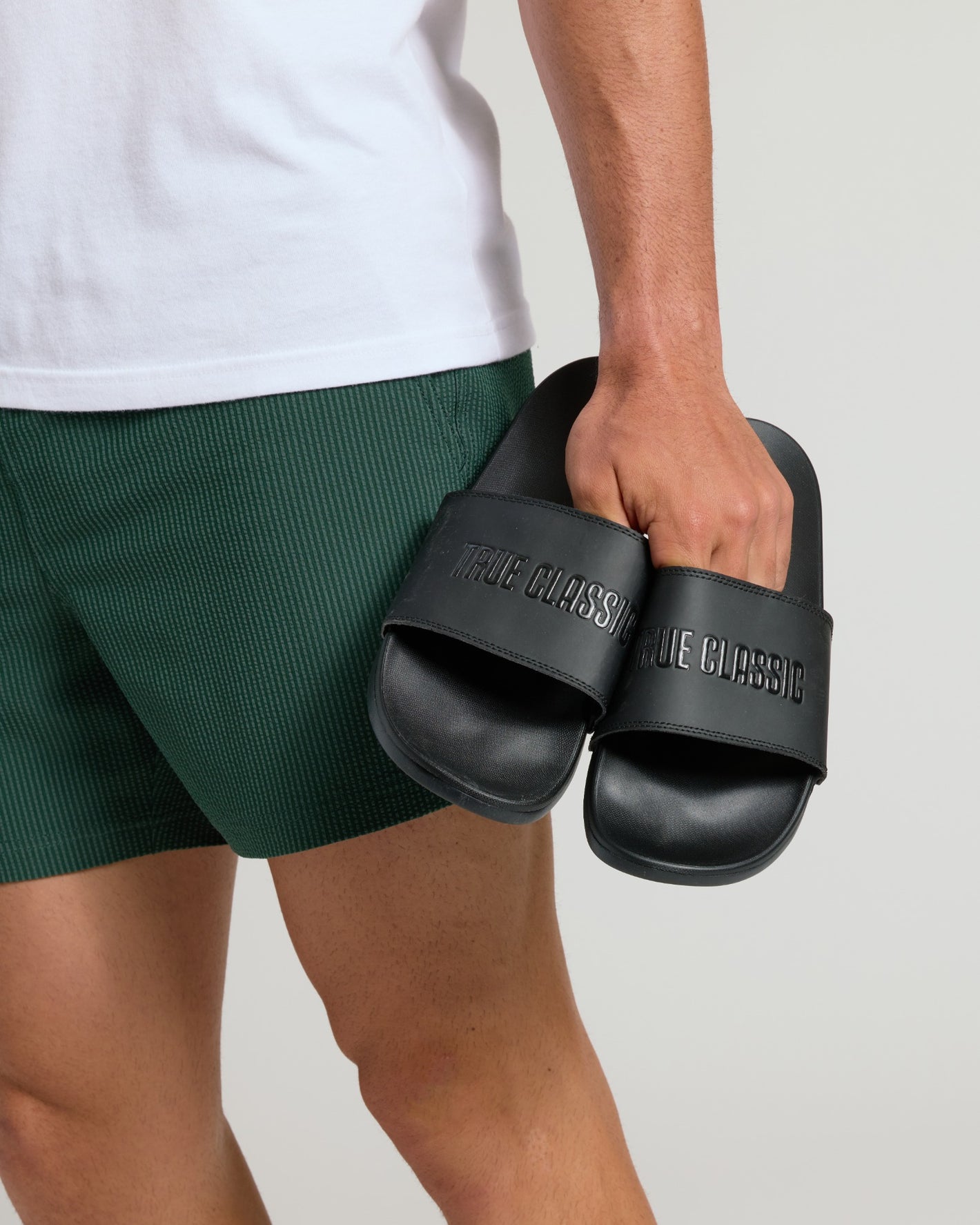 Person holding Black Comfort Slides with TRUE CLASSIC on straps.
