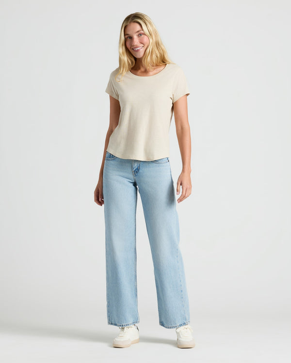 Woman wearing a beige t-shirt and light blue jeans on a white background