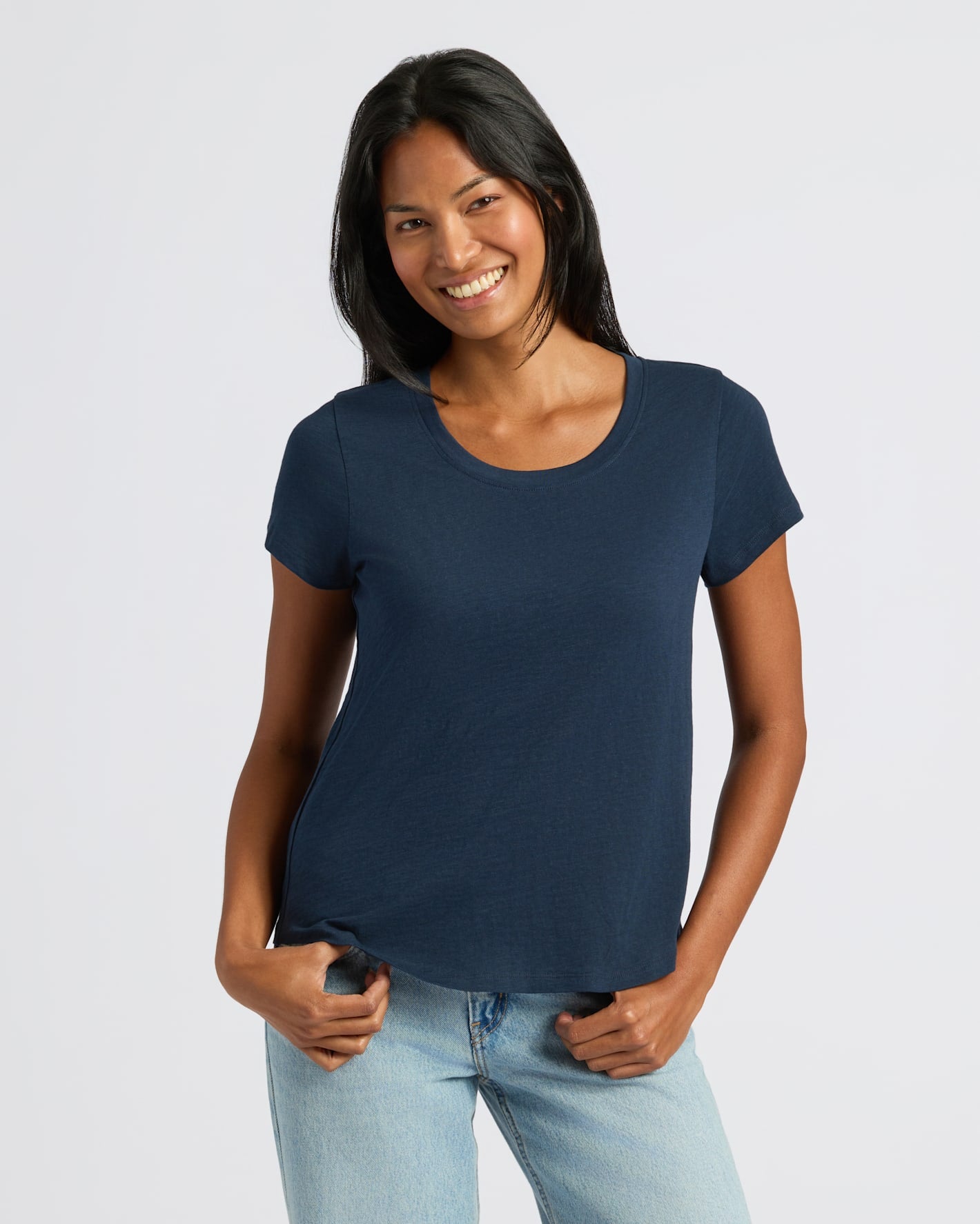 Woman wearing a navy blue t-shirt and light blue jeans on a white background