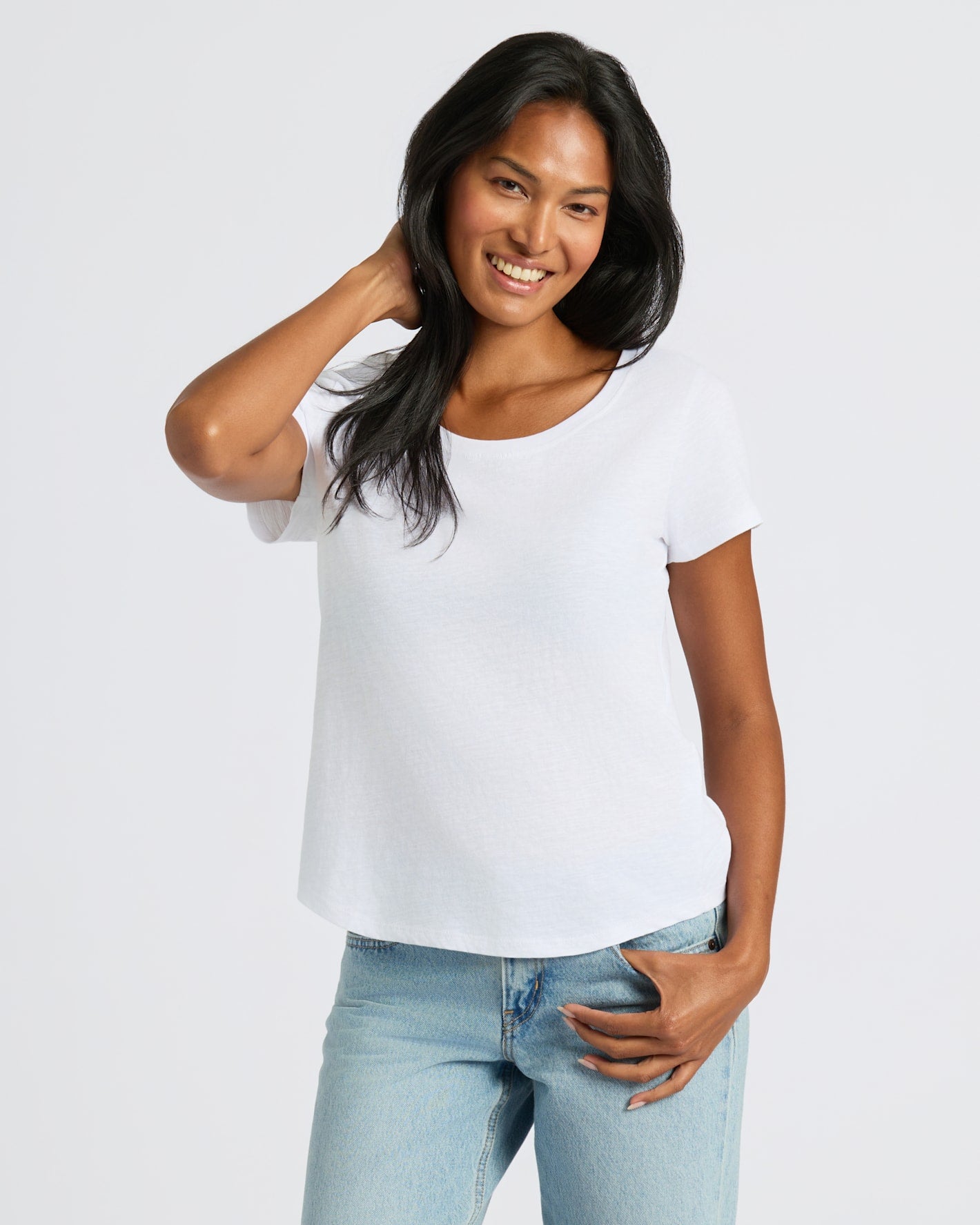 Woman wearing a white t-shirt and blue jeans on a plain background