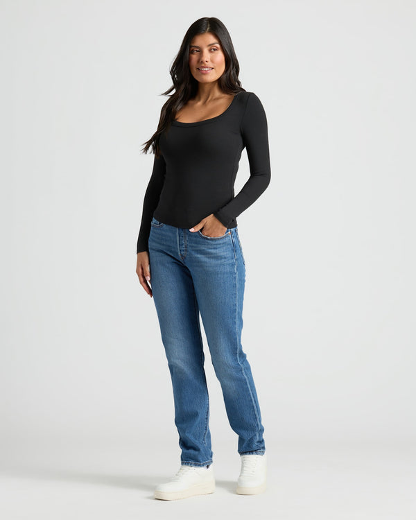 Woman wearing a black long-sleeve top and blue jeans on a white background