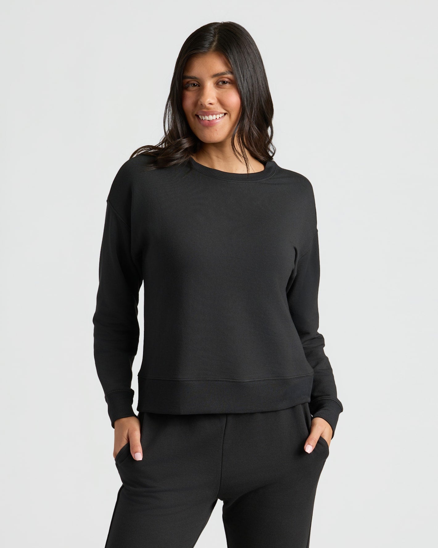 Woman wearing a black sweatshirt and pants on a light gray background