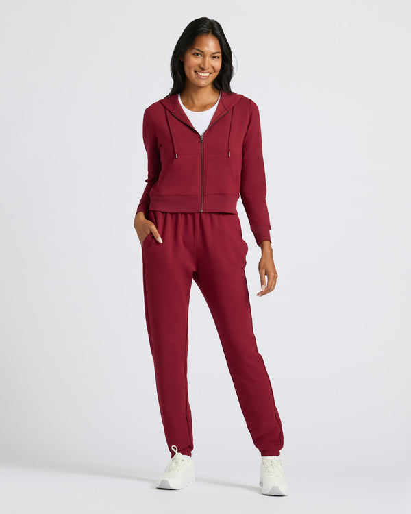 Model in Womens Dark Maroon Crop Zip Hoodie, smiling with hand in pocket.