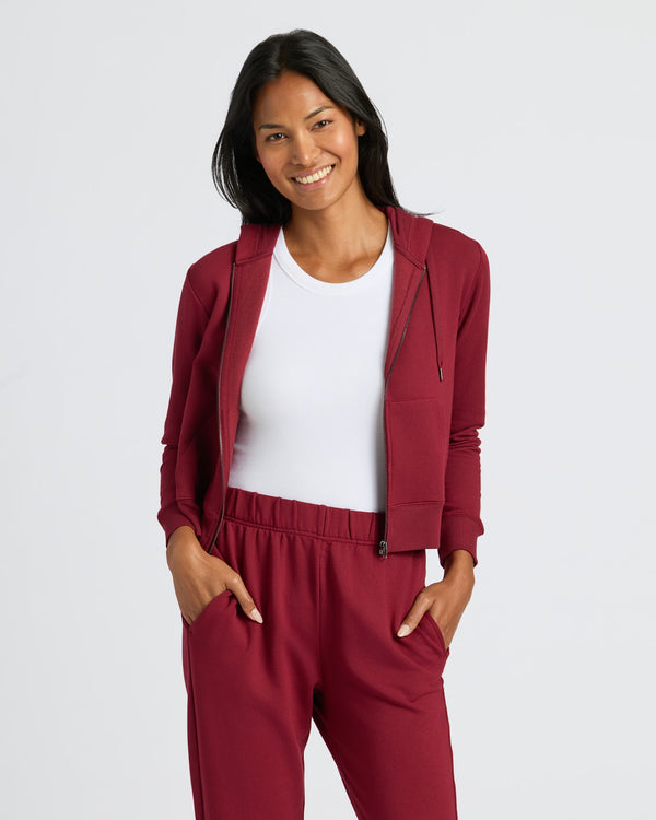 Woman wearing Womens Dark Maroon Crop Zip Hoodie, smiling, hands in pockets. MODEL_INFO: Candy is 5'9", wearing a size S