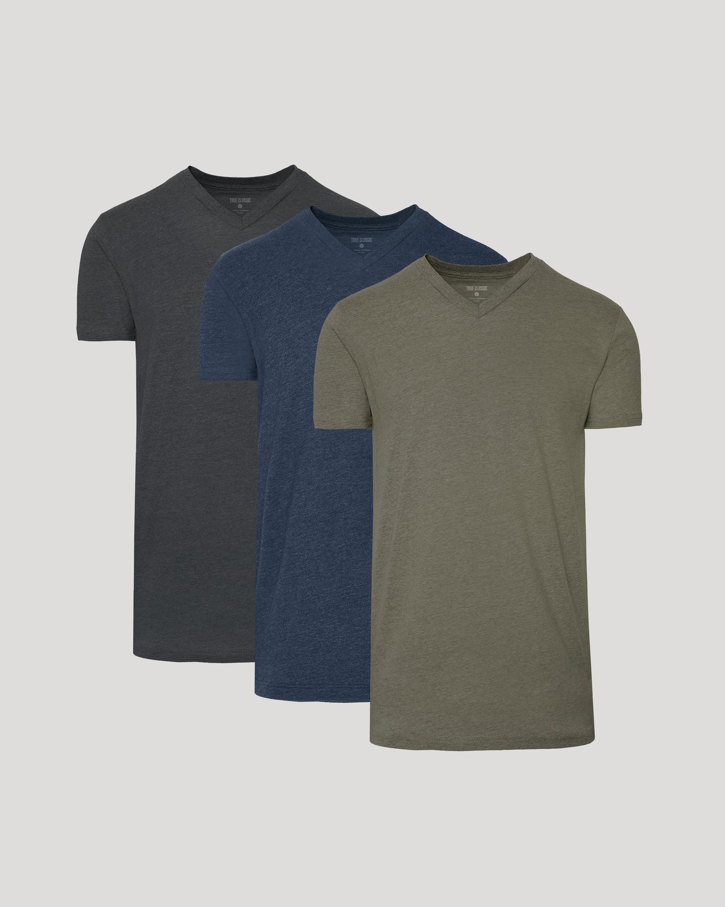 Three plain t-shirts in black, blue, and green on a light gray background