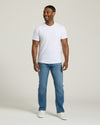 Man wearing a white t-shirt and blue jeans on a plain background