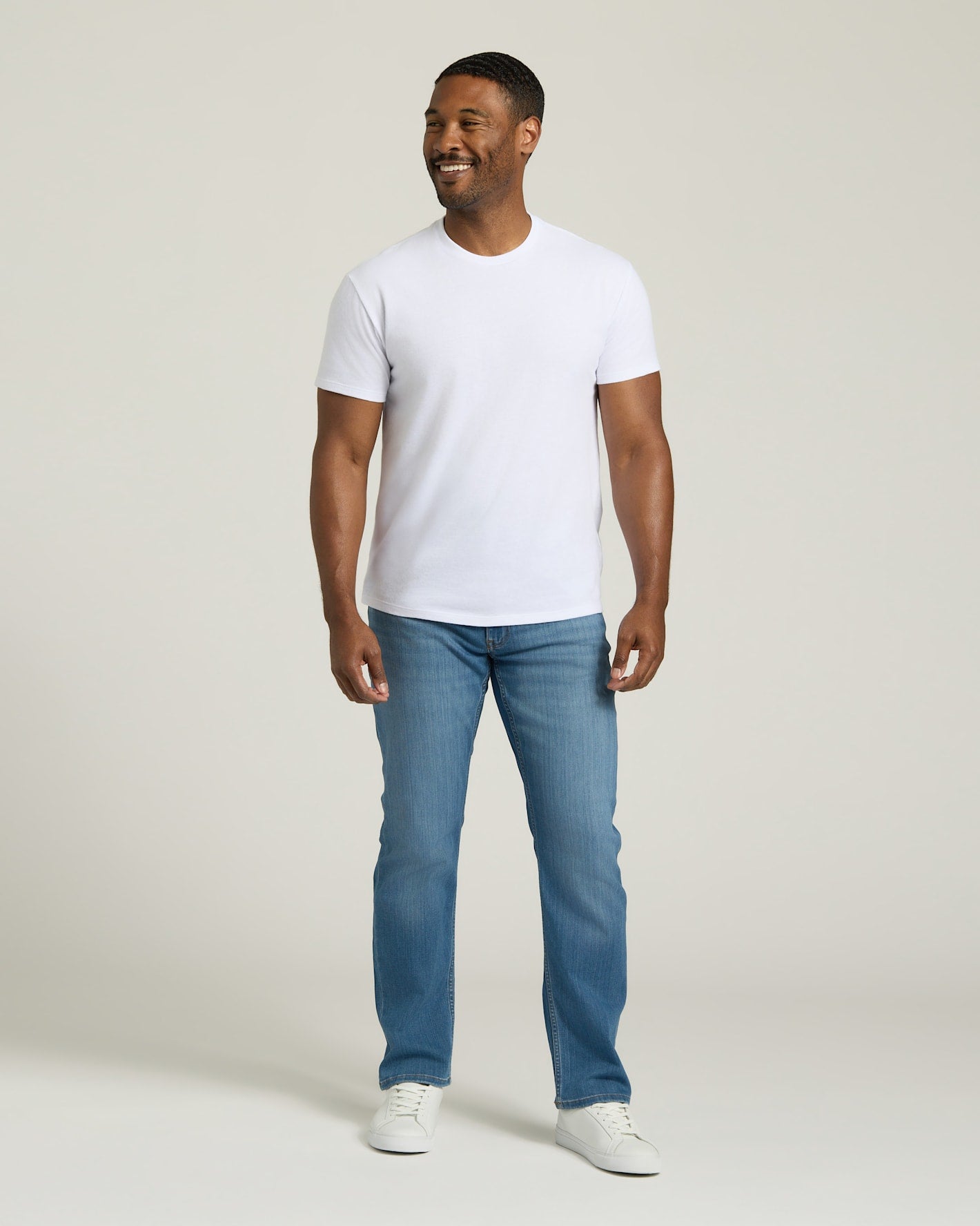 Man wearing a white t-shirt and blue jeans on a plain background