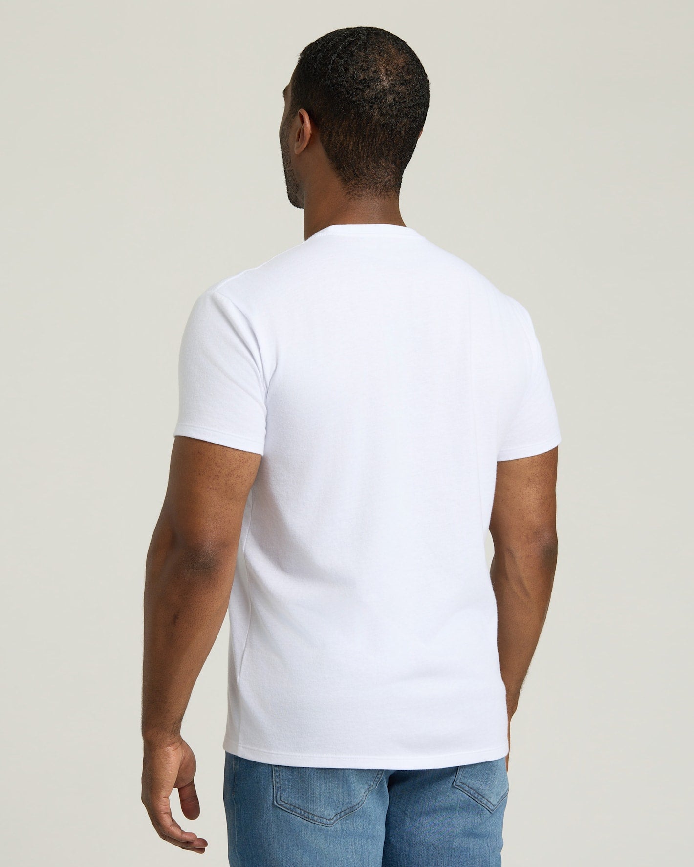 Man wearing a plain white t-shirt and blue jeans against a light background