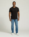 Man wearing a black t-shirt, blue jeans, and white sneakers on a plain background