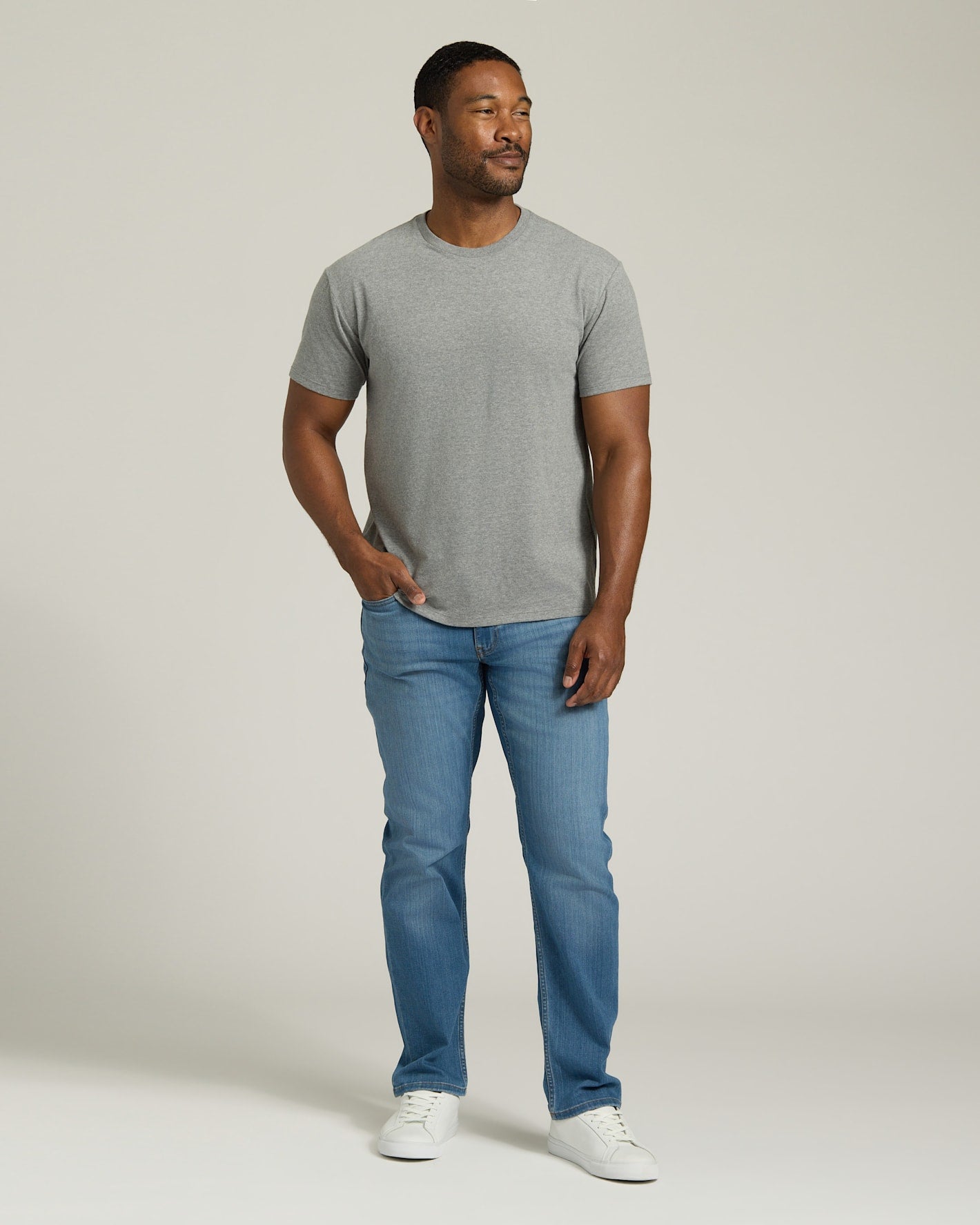 Man wearing a gray t-shirt and blue jeans standing against a plain background