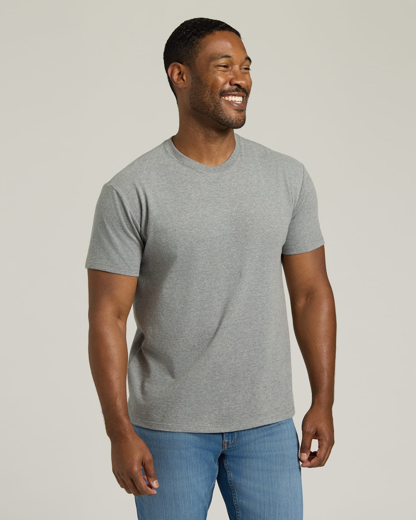 Man wearing a gray t-shirt and blue jeans against a plain background