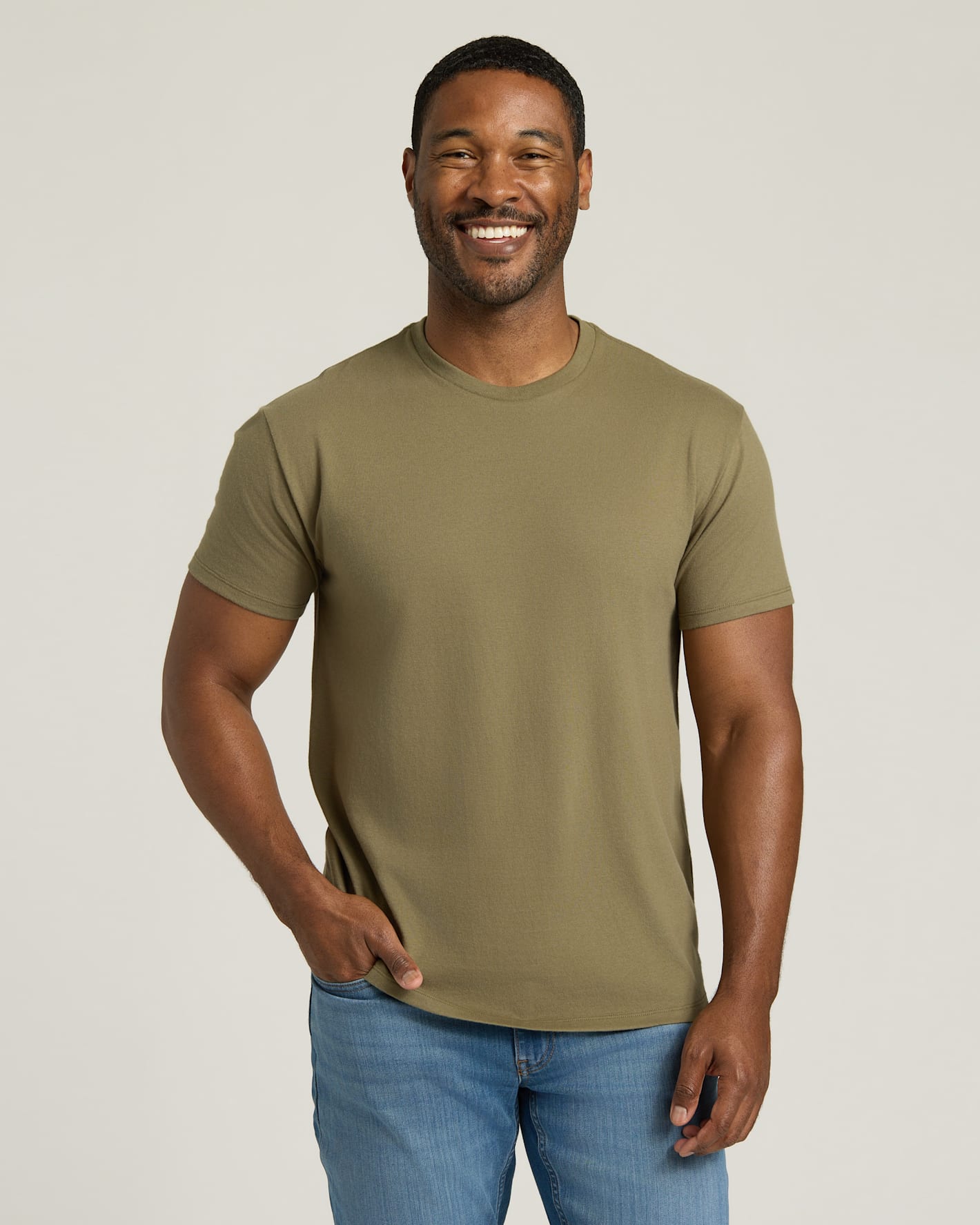 Man wearing an olive green t-shirt and blue jeans against a plain background