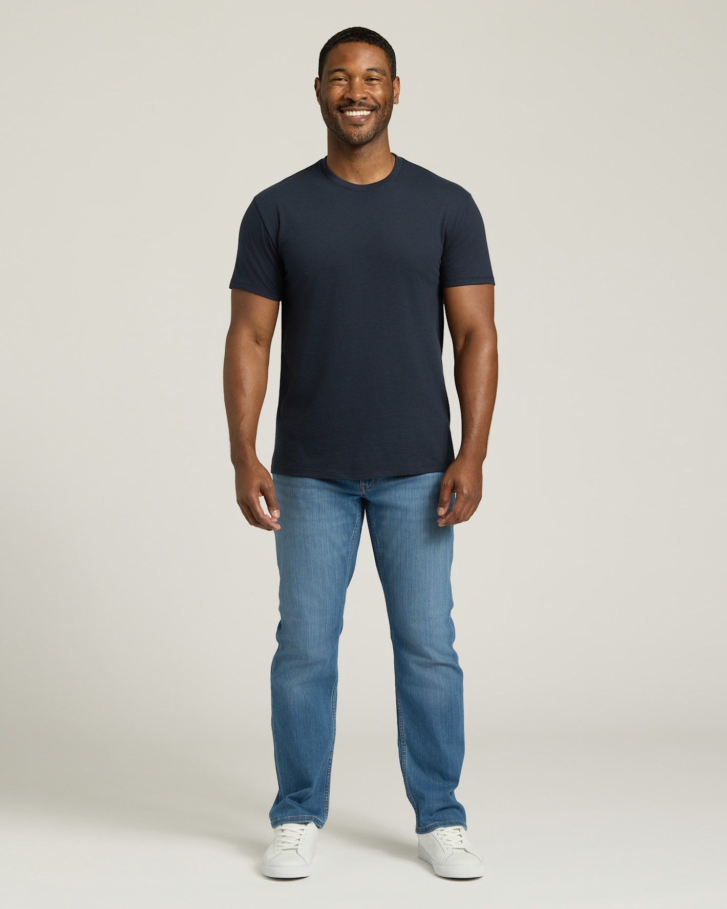Man wearing a navy t-shirt and blue jeans on a white background