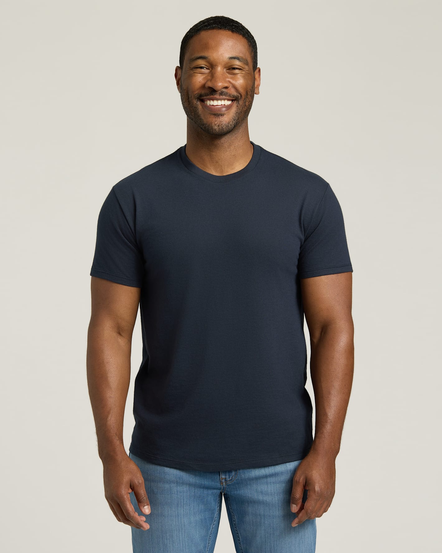 Man wearing a navy blue t-shirt and blue jeans against a plain background