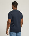 Man wearing a navy blue t-shirt and light blue jeans on a plain background
