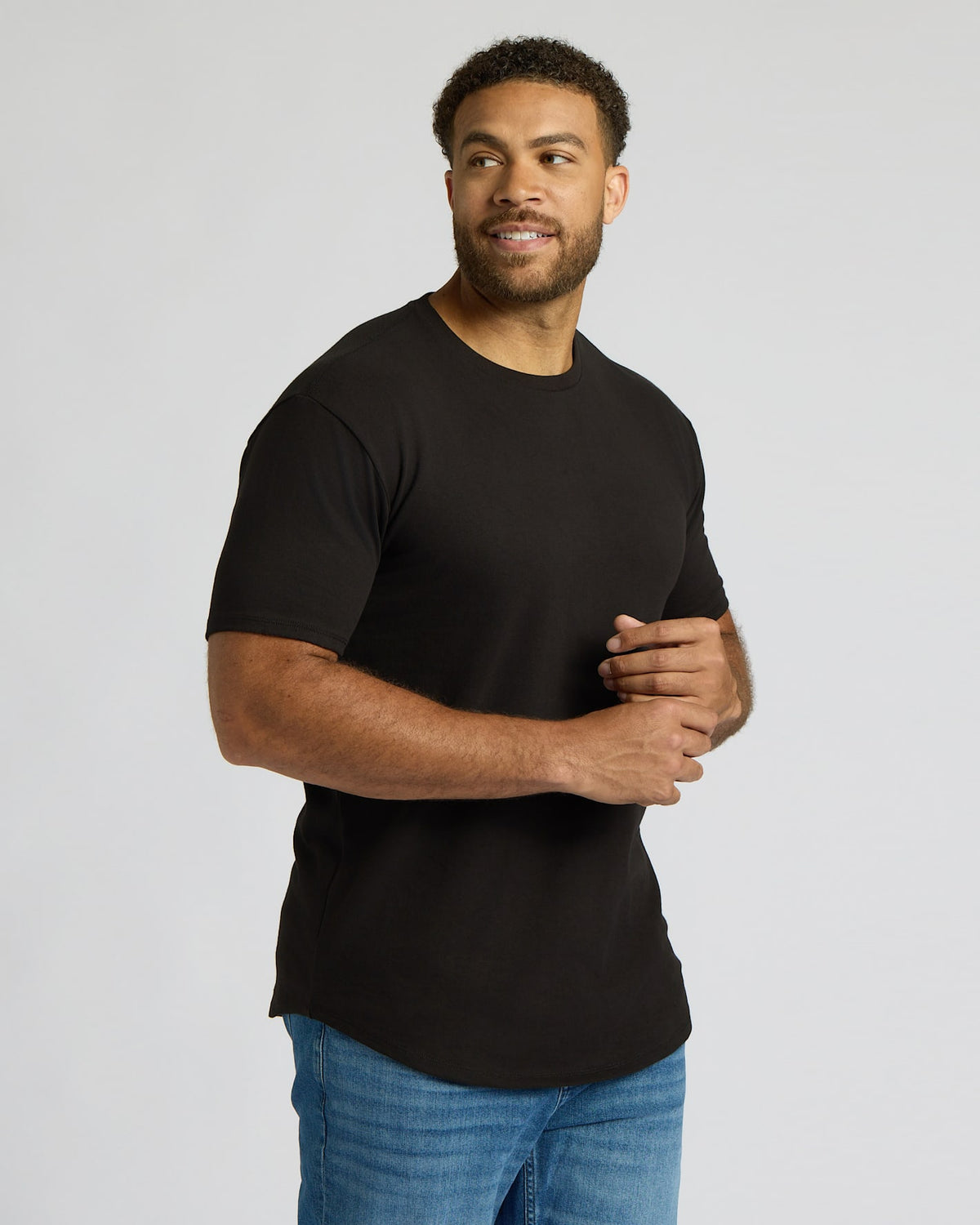 Man wearing a black True Classic Men's Tall Heavyweight Curved Hem Crew – Premium Heavyweight Cotton Blend, Extended Length, Athletic Fit, Structured Everyday T-Shirt with blue jeans against a plain background.