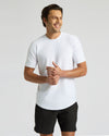 A smiling man wearing a white Active Curved Hem Crew Tee - Men's Moisture Wicking Performance T-Shirt paired with black shorts, showcasing a casual and comfortable men's basics look.