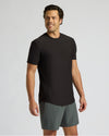 Man wearing a black Active Curved Hem Crew Tee - Men's Moisture Wicking Performance T-Shirt with curved hem and short sleeves, paired with gray shorts against a plain background.