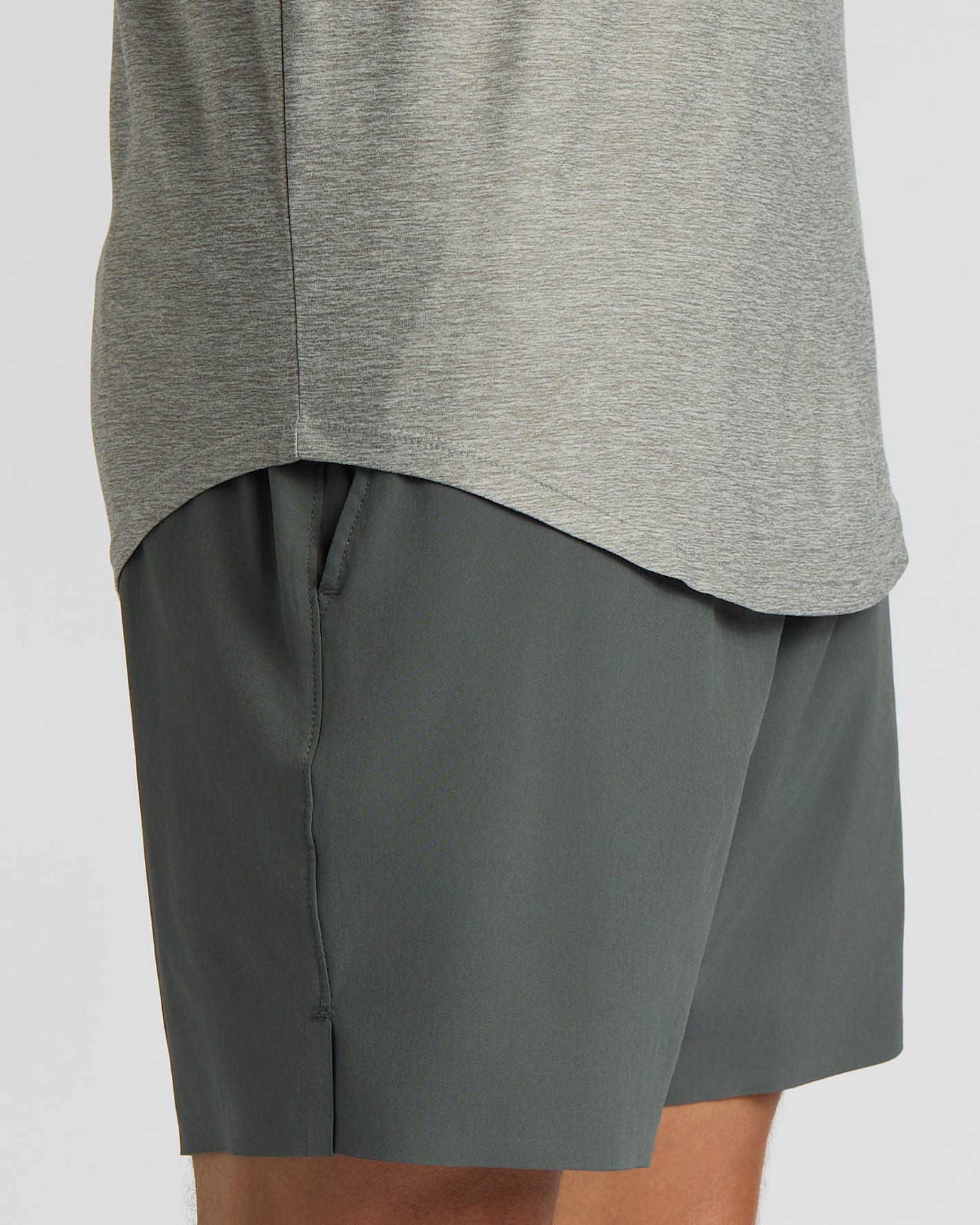 Close-up of a person wearing heather gray athletic shorts and the lower portion of a gray long-sleeve top against a light gray studio background.