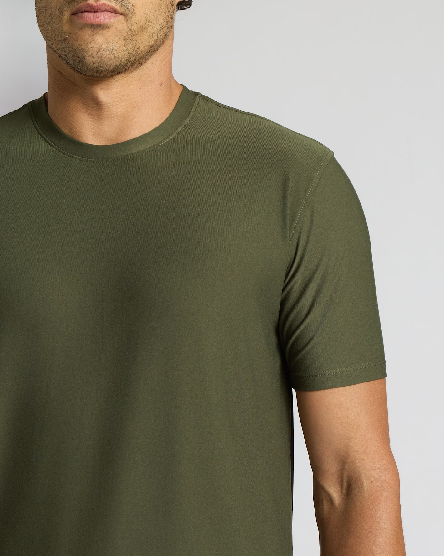 A close-up of a man wearing a solid olive green crew-neck t-shirt against a light gray background.