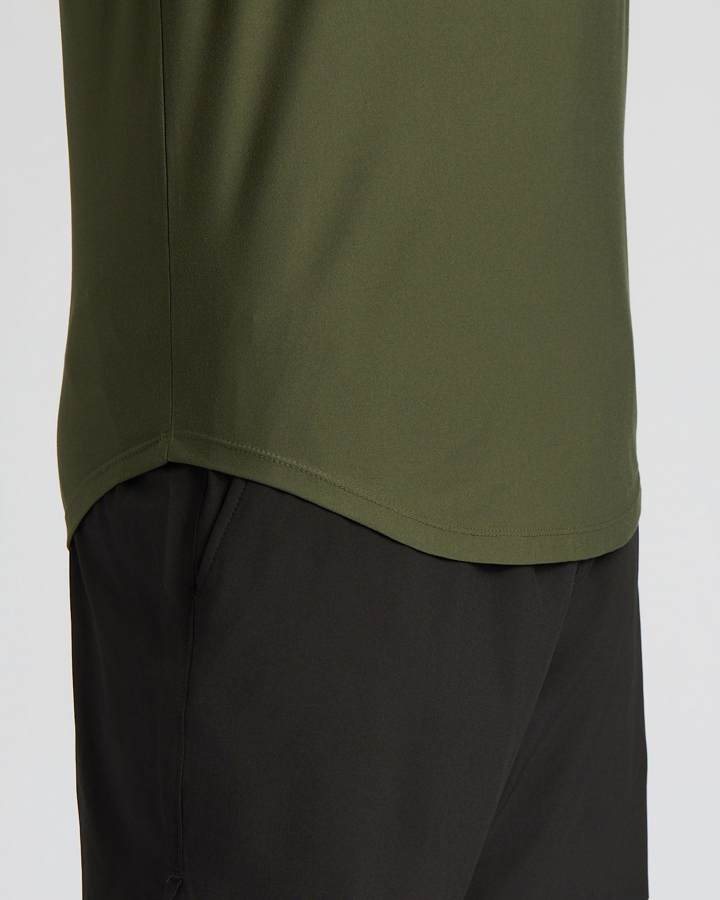 Close-up of a person wearing an olive green athletic top and black shorts against a light gray background.