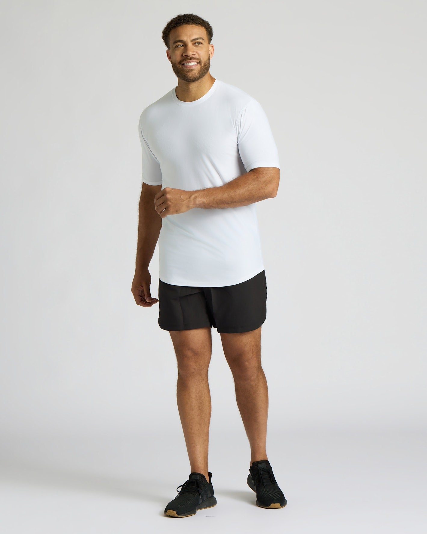 Man wearing a white t-shirt and black shorts on a light gray background